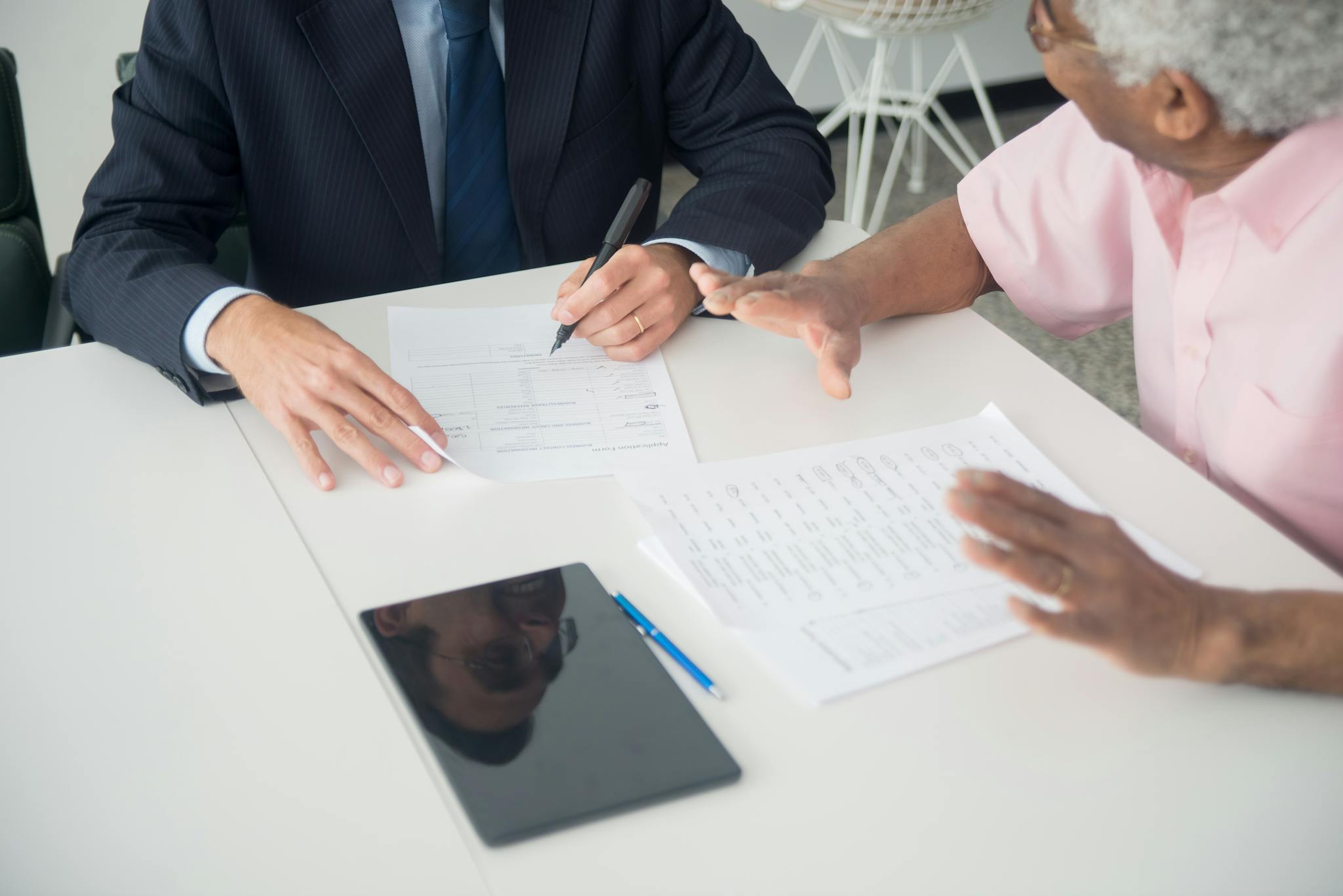 A business meeting between an elderly client and a consultant discussing documents at an office table.